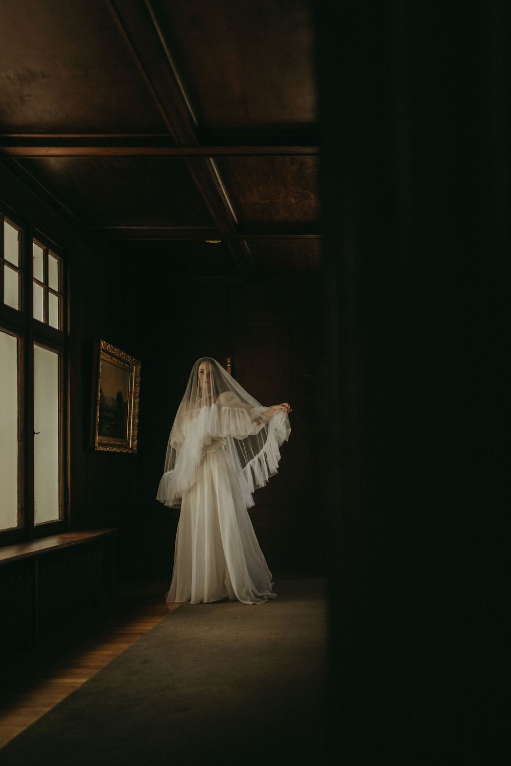 Artistic silhouette of a bride in a flowing white dress walking through a dimly lit hallway.