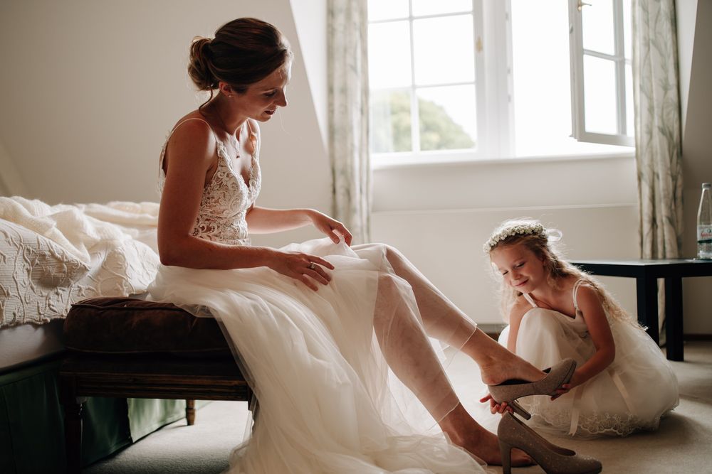 A heartwarming moment captured during wedding preparations as a bride and young attendant sit together in a sunlit room.Weiherhof Wächtersba