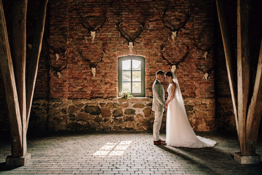 A couple shares a romantic moment in a rustic stone room with antler decorations and natural light Weiherhof Wächtersbach
