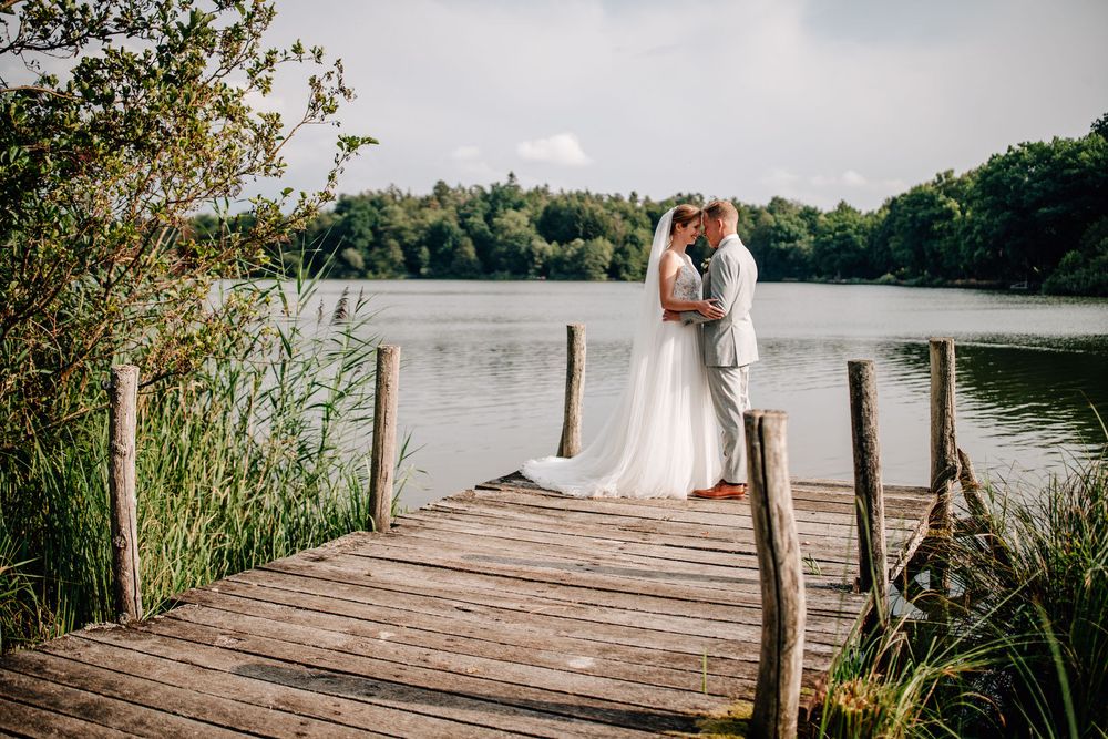 Wedding couple embracing on a wooden dock overlooking a serene lake during sunset.Weiherhof Wächtersbach
