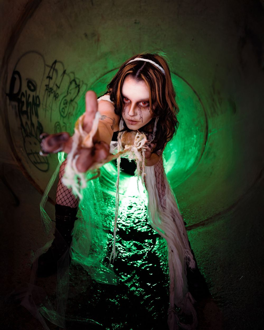 a woman with spider inspired makeup and costuming in a drainage tunnel in a horror inspired photoshoot