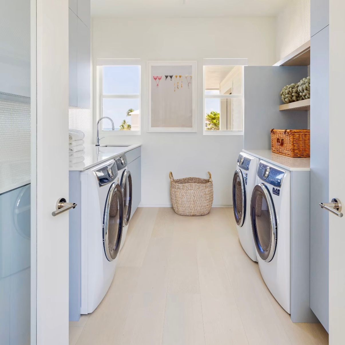 Modern white laundry room with multiple front-loading washers and dryers in neat row against wall with storage shelves.