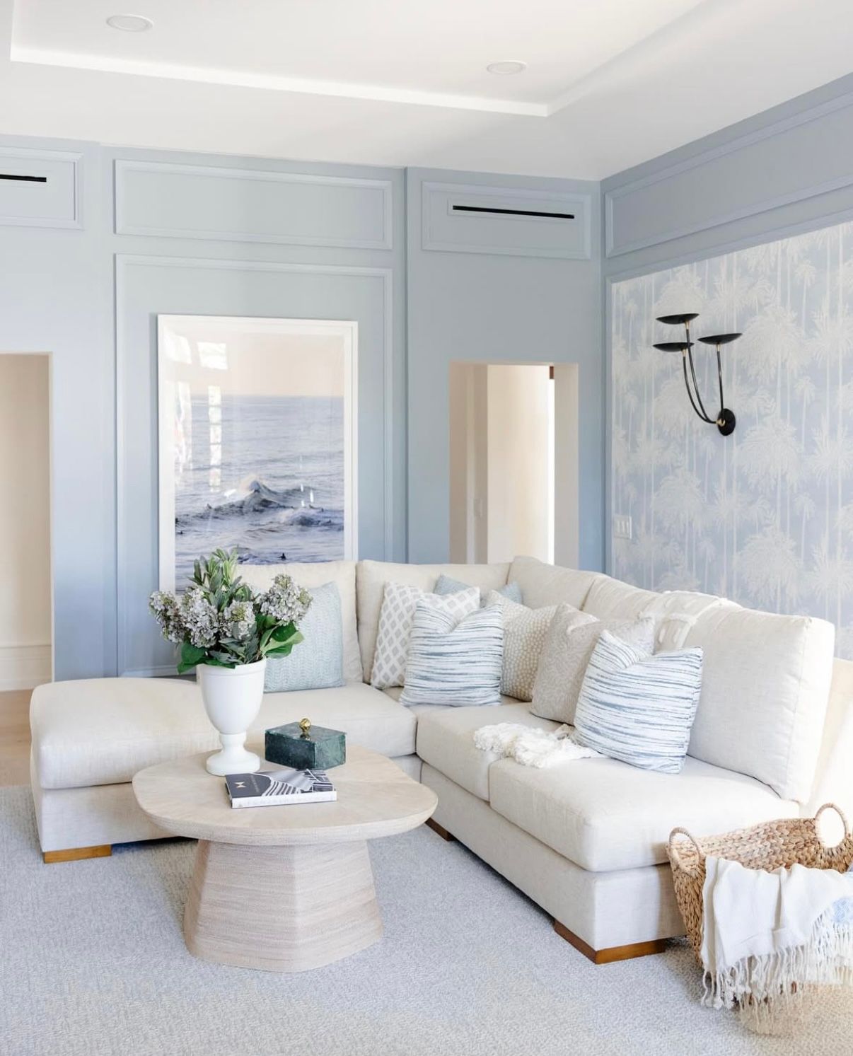Modern living room with white sofas, light blue walls, and stylish coastal decor arranged in a gallery-style layout.