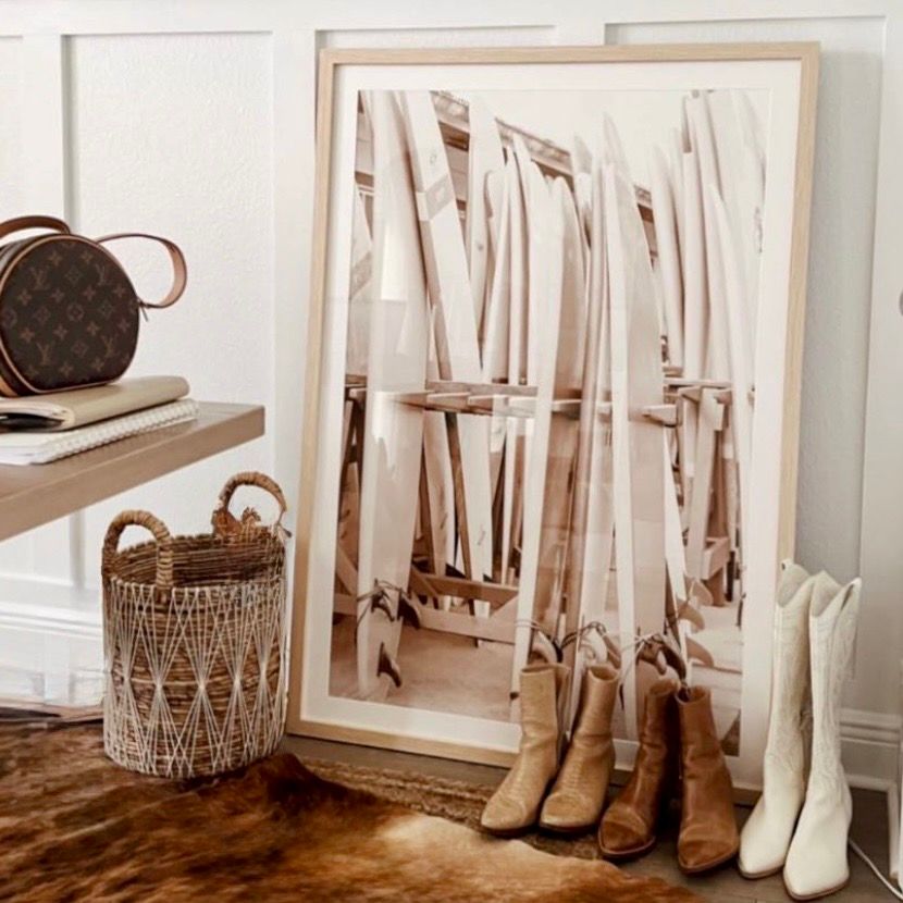 Neutral boho entryway with framed art, wicker basket, Louis Vuitton bag, tan and white cowboy boots on cowhide rug.