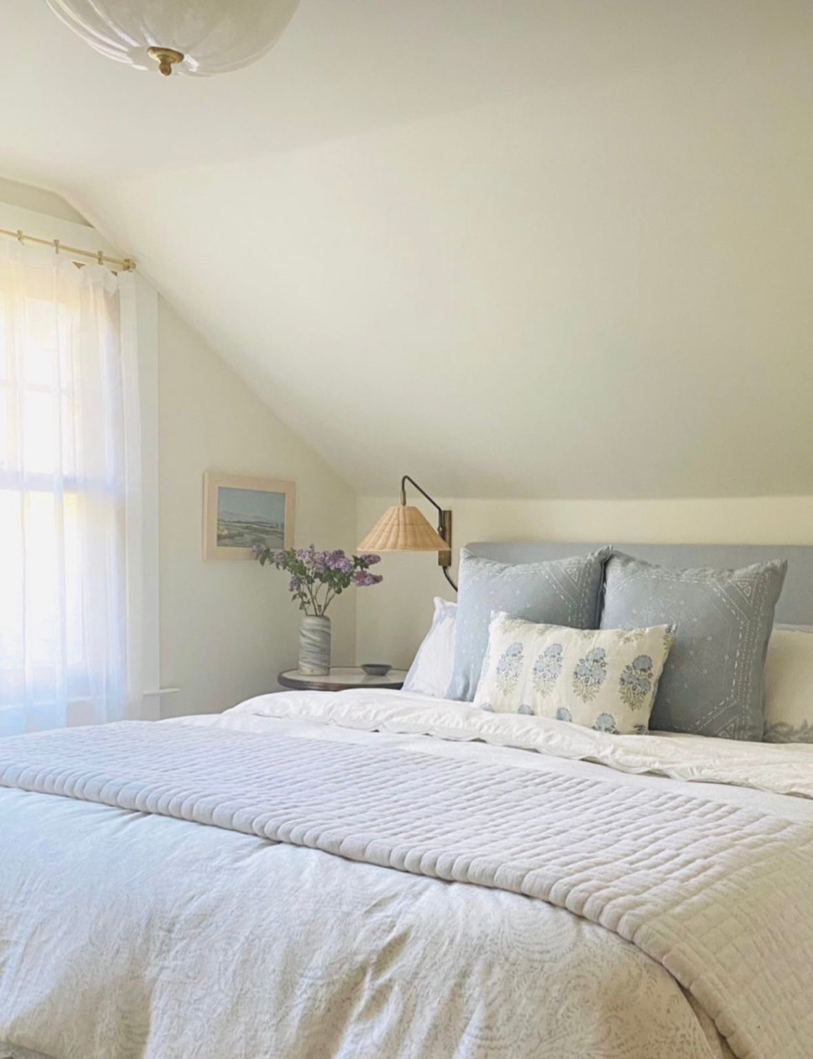 White bedding with soft textural details creates a cozy and inviting bedroom atmosphere with natural light streaming in.
