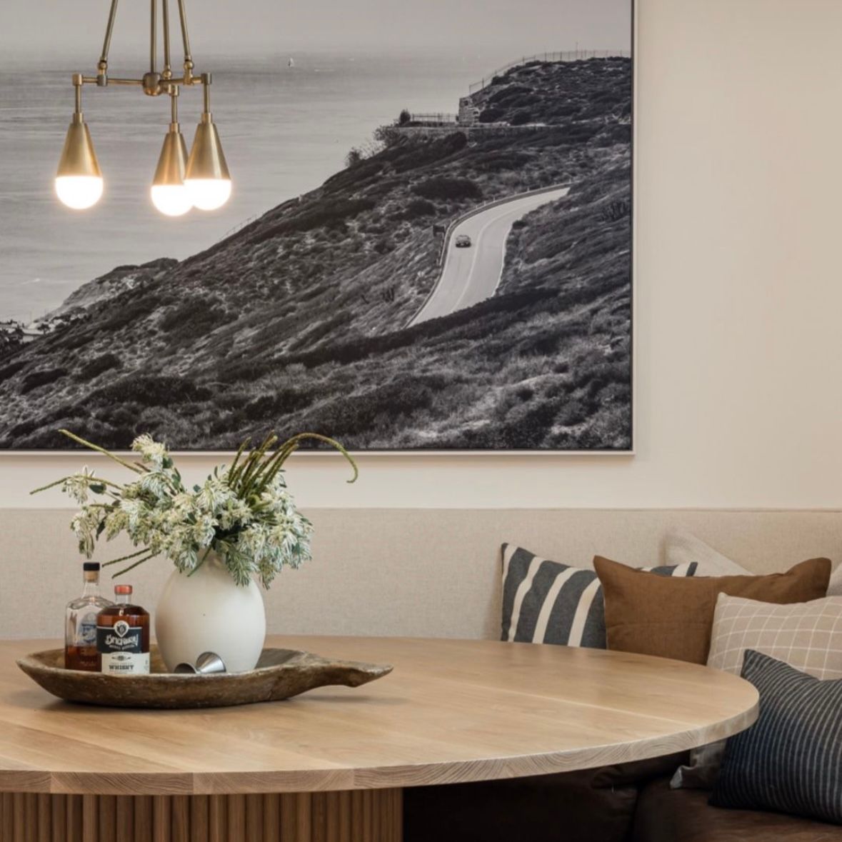 Modern dining area with round wooden table, pendant lights, and black and white landscape artwork on light gray walls.