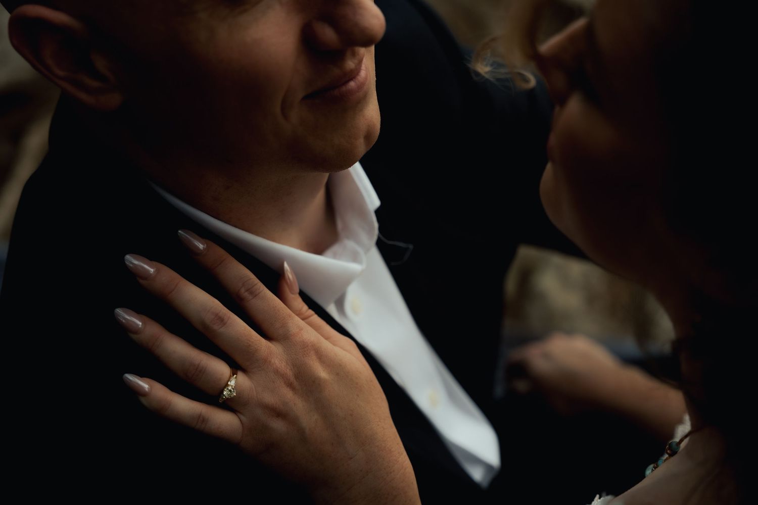 A close-up shot of two people embracing with a sparkly engagement ring prominently displayed on one hand.