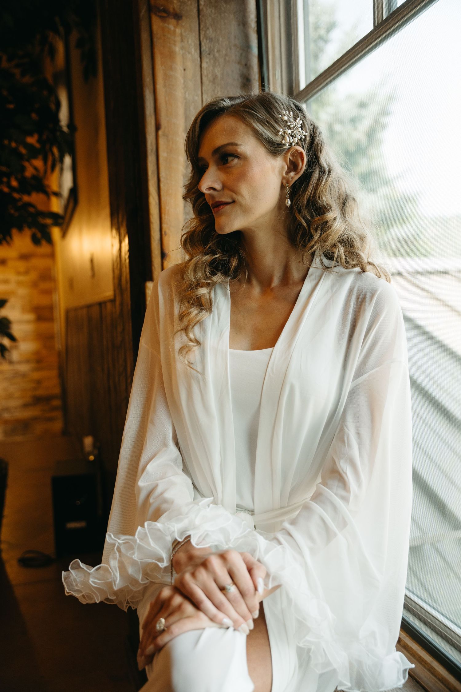 A woman in a white silk robe gazes thoughtfully out of a window in a series of romantic boudoir photos.