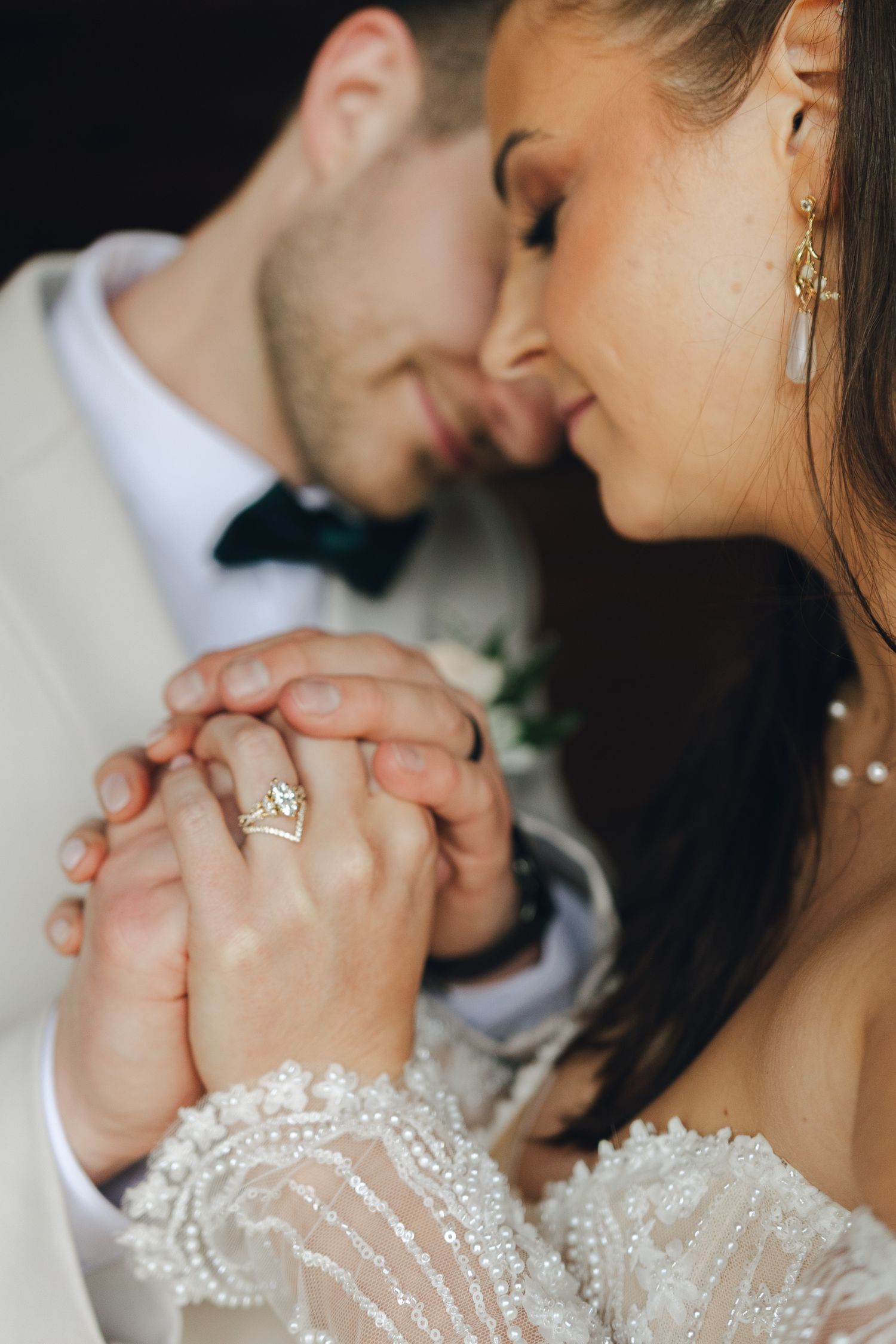 Close-up of newlywed couple holding hands showing delicate lace wedding dress details and romantic intimacy.