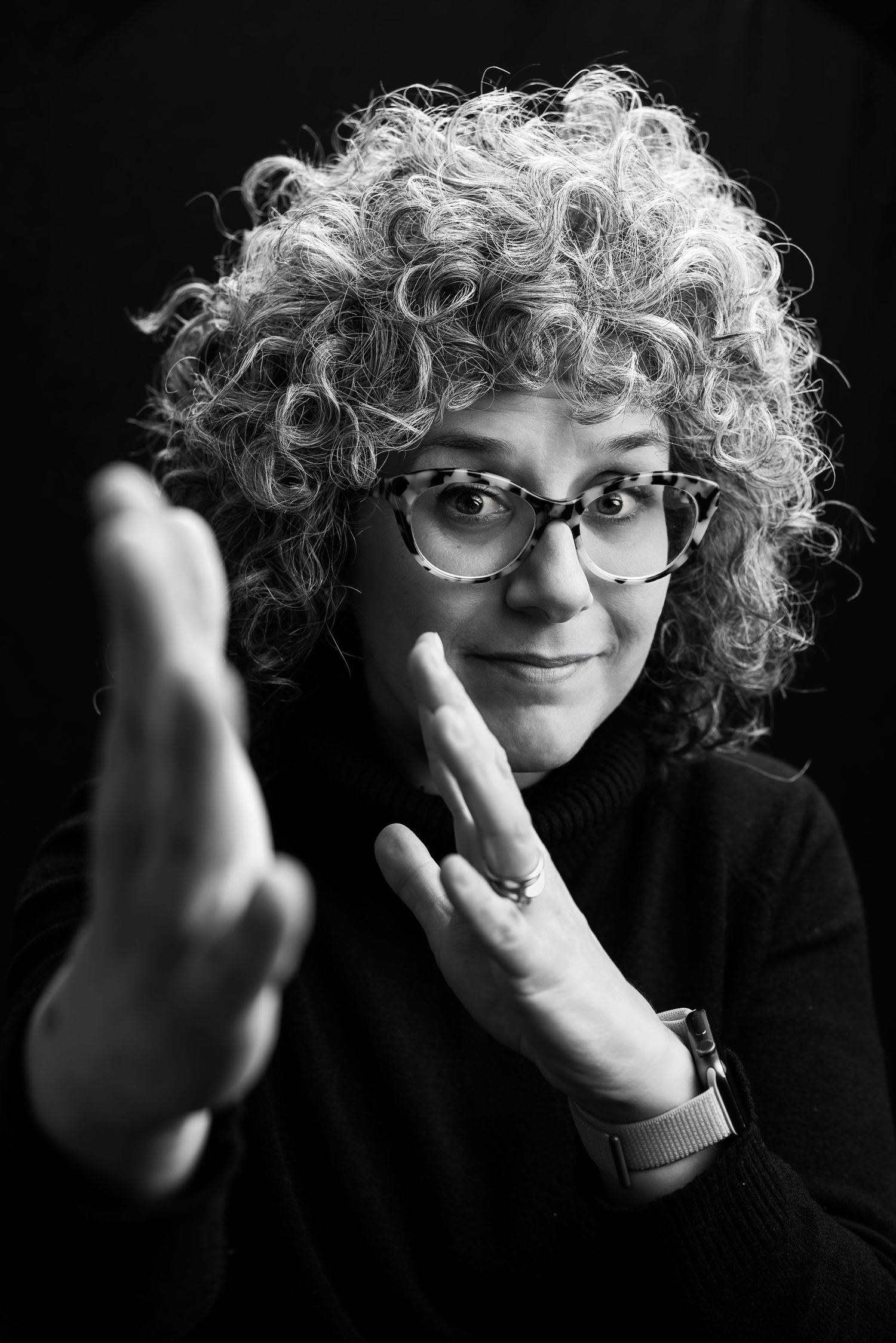 Dramatic black and white portrait showcasing curly hair, glasses, and contemplative pose.