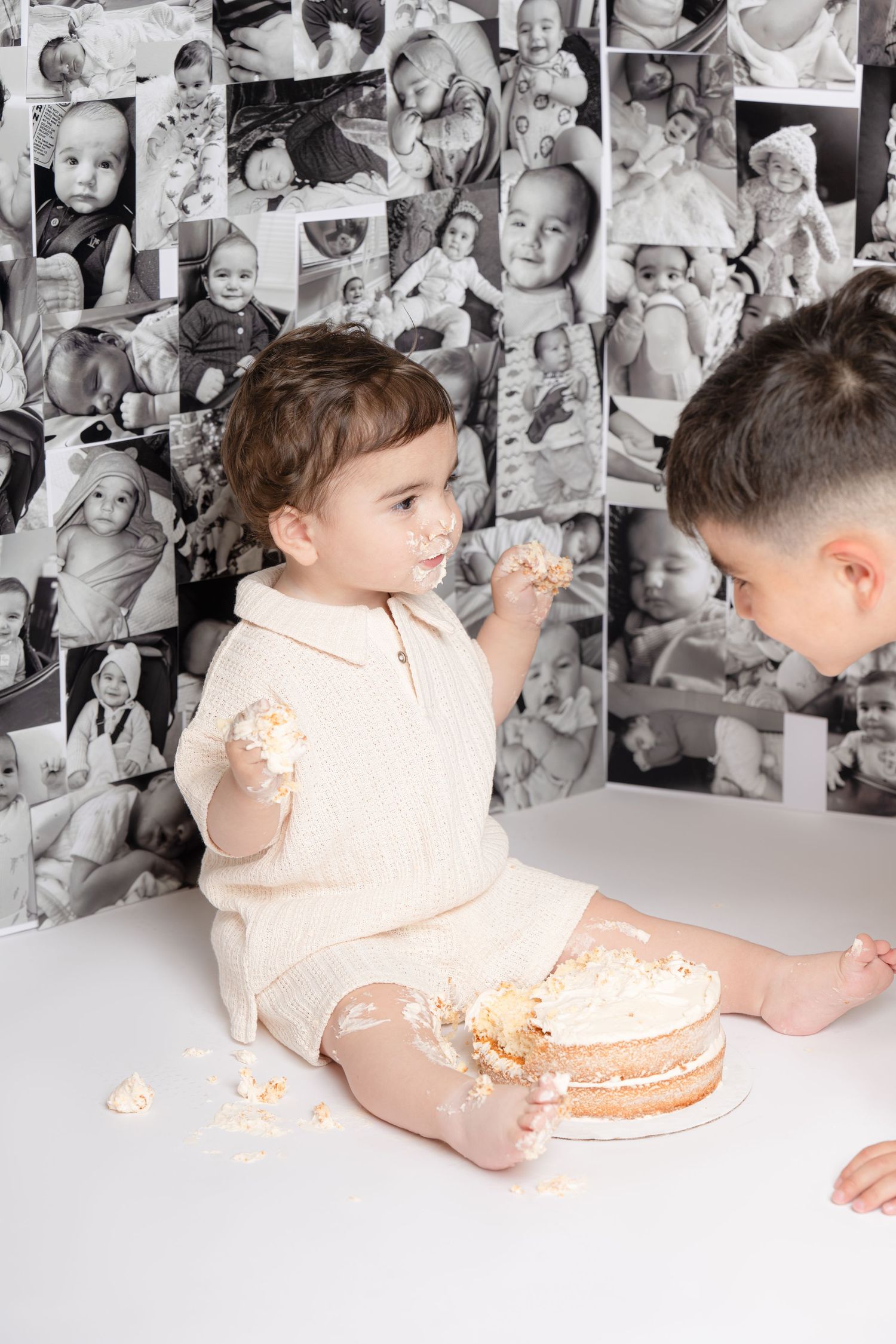 Young child celebrating with a birthday cake during a cake-smash photoshoot as another child leans in.