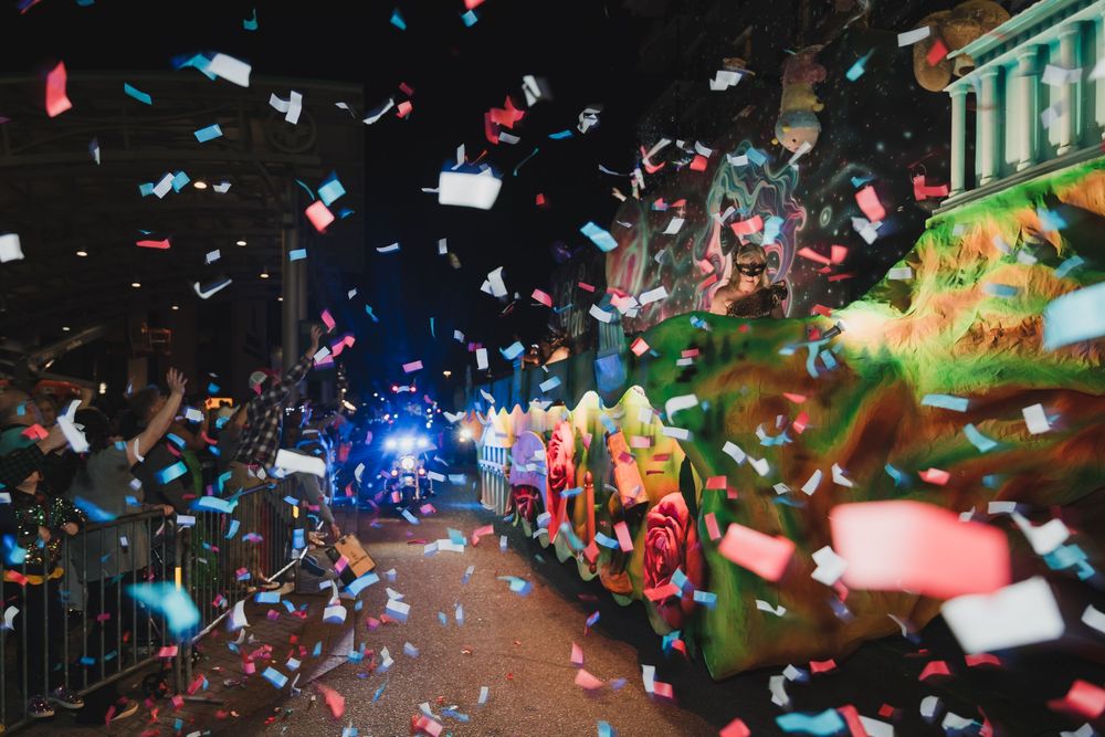 Colorful confetti fills the night sky above a festive parade float on a decorated street during a celebration.