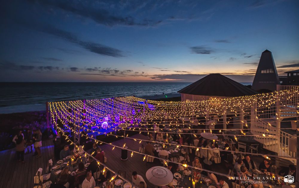 Stunning sunset view of Bud n' Ally's in Seaside, FL with rows of illuminated purple lights leading to the ocean.