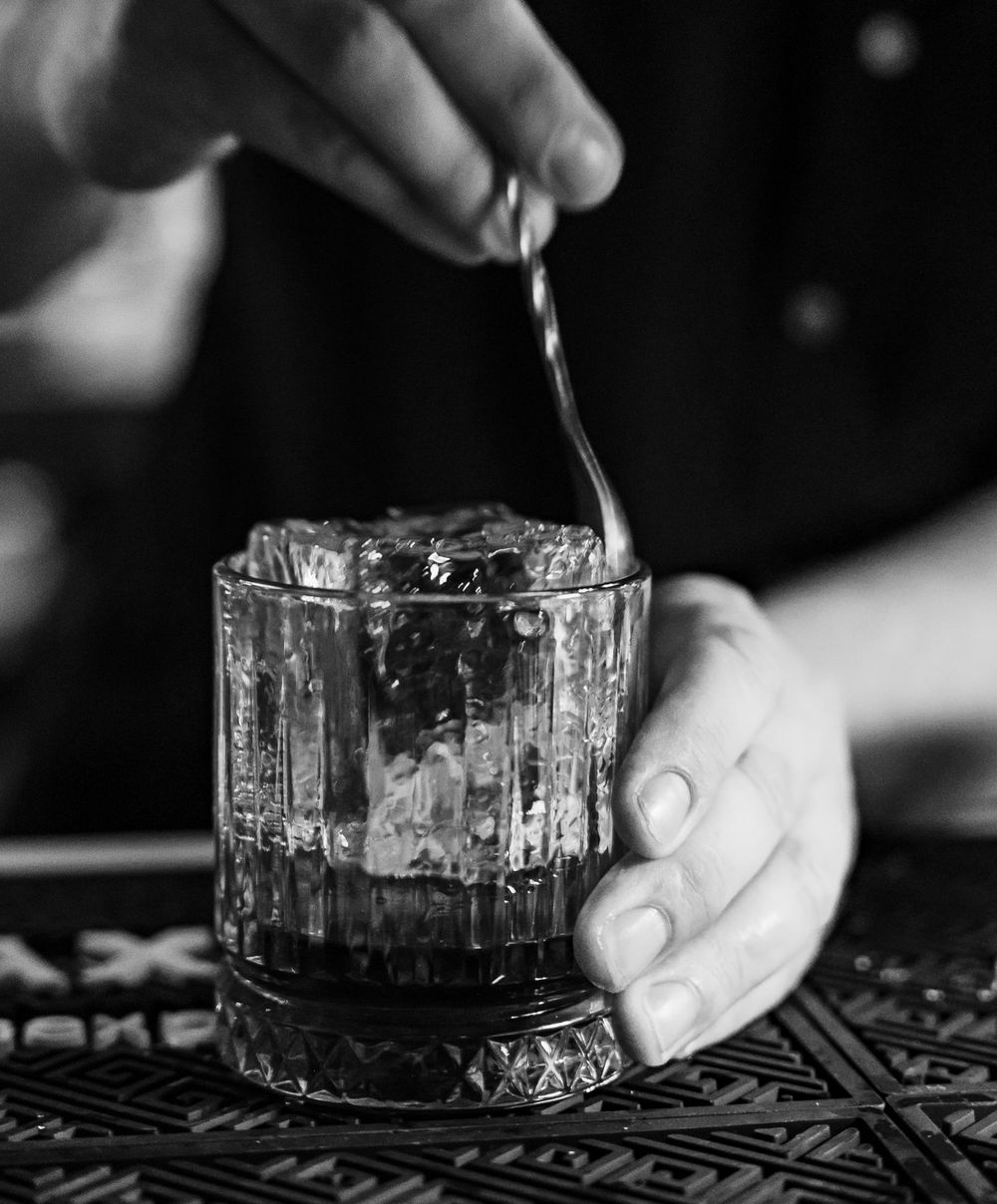Close-up of hands stirring a cocktail in a crystal glass.