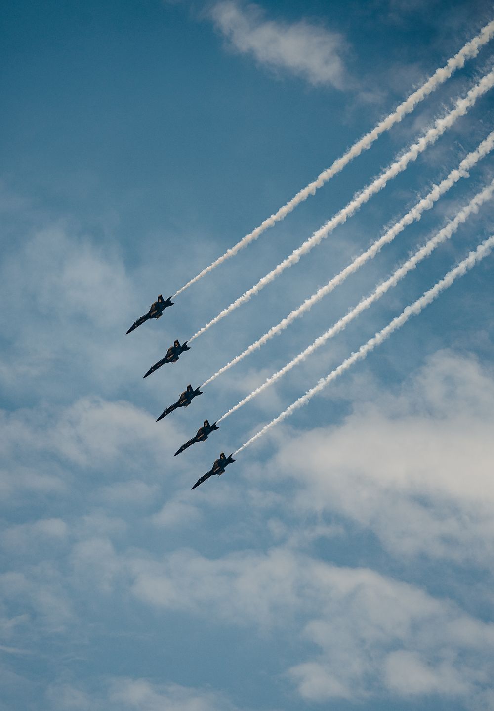 The Blue Angels flying in diagonal formation leaving white contrails against blue sky.