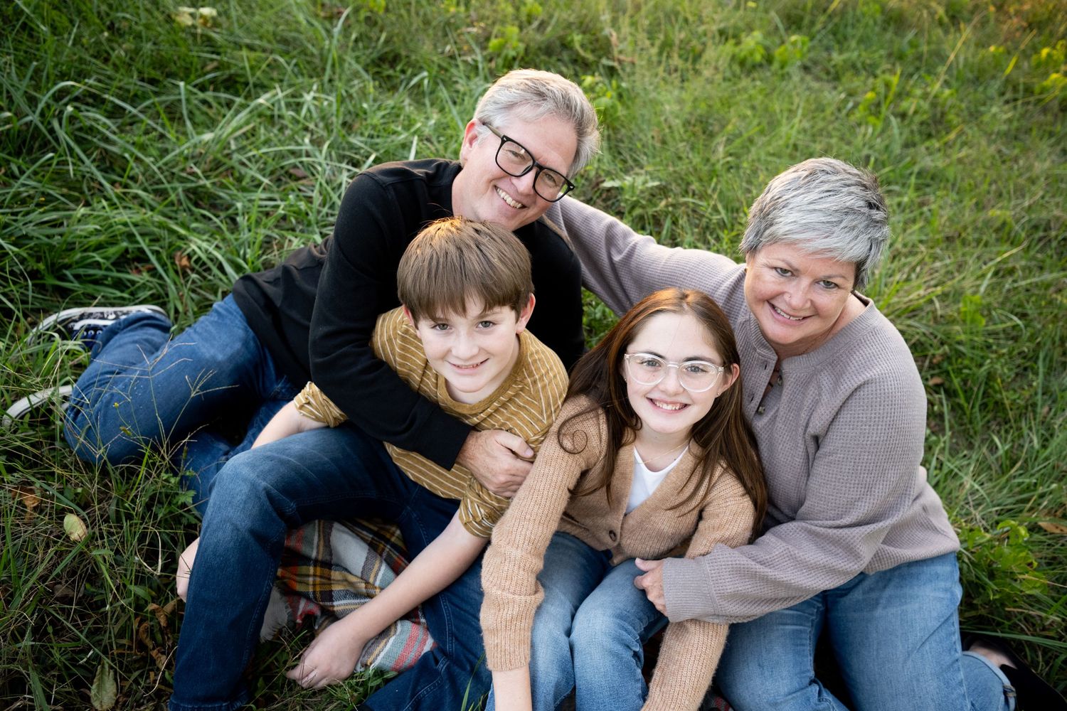 Family of four sitting close together on grass smiling at camera.