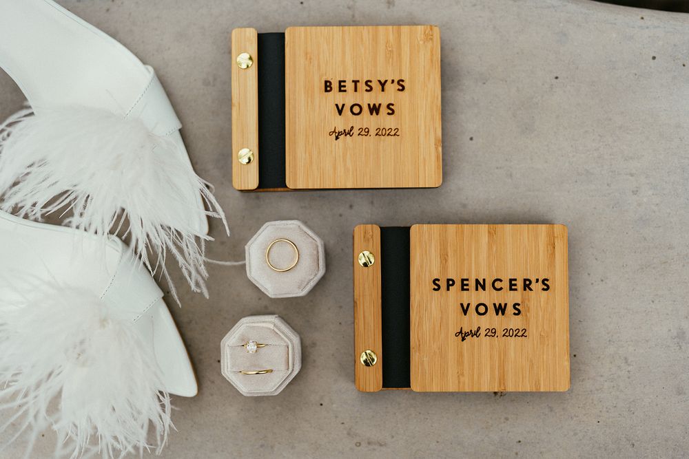 Wooden vow books with names engraved alongside white feathers and rings.