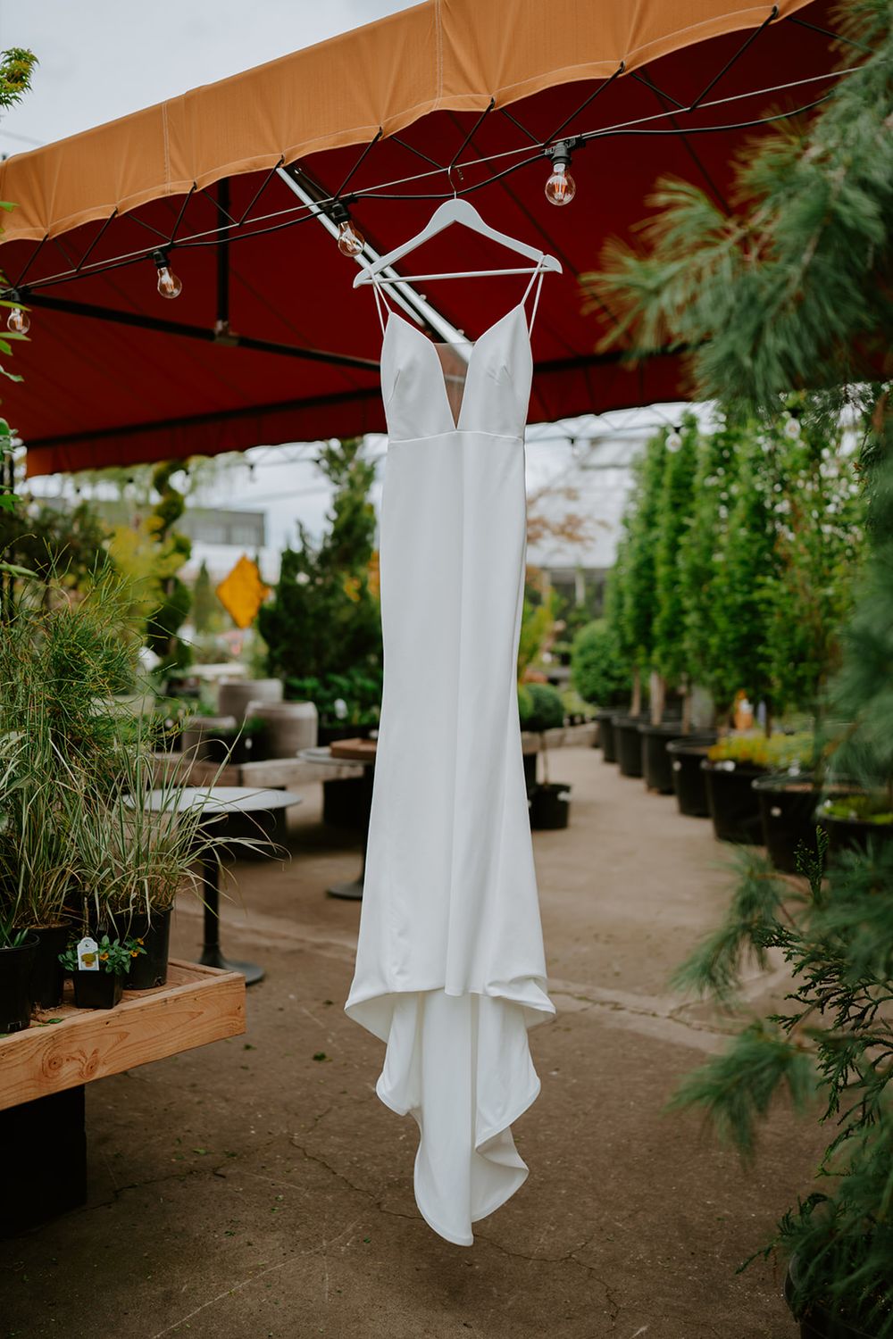 Sleek white wedding dress hanging on display in an outdoor garden setting.