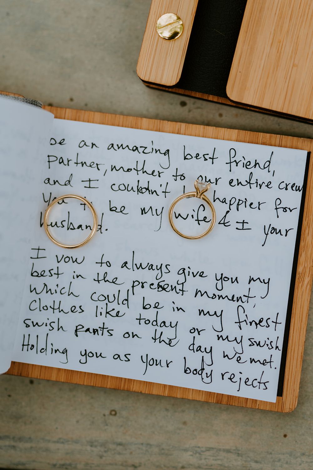 Handwritten wedding vows with gold wedding rings on wooden surface.