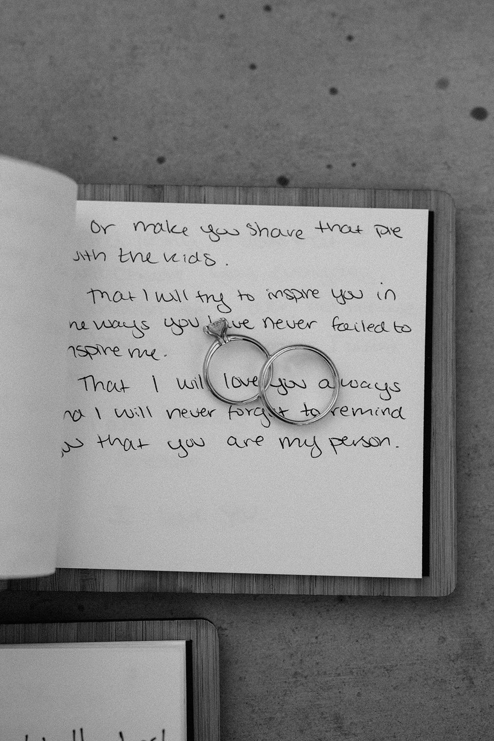 Black and white photo of handwritten wedding vows with ring casting shadow on paper.