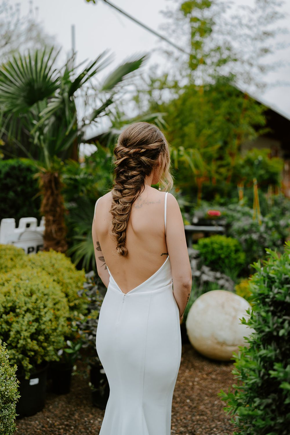 Elegant backless wedding dress with intricate braided hairstyle in a garden setting.