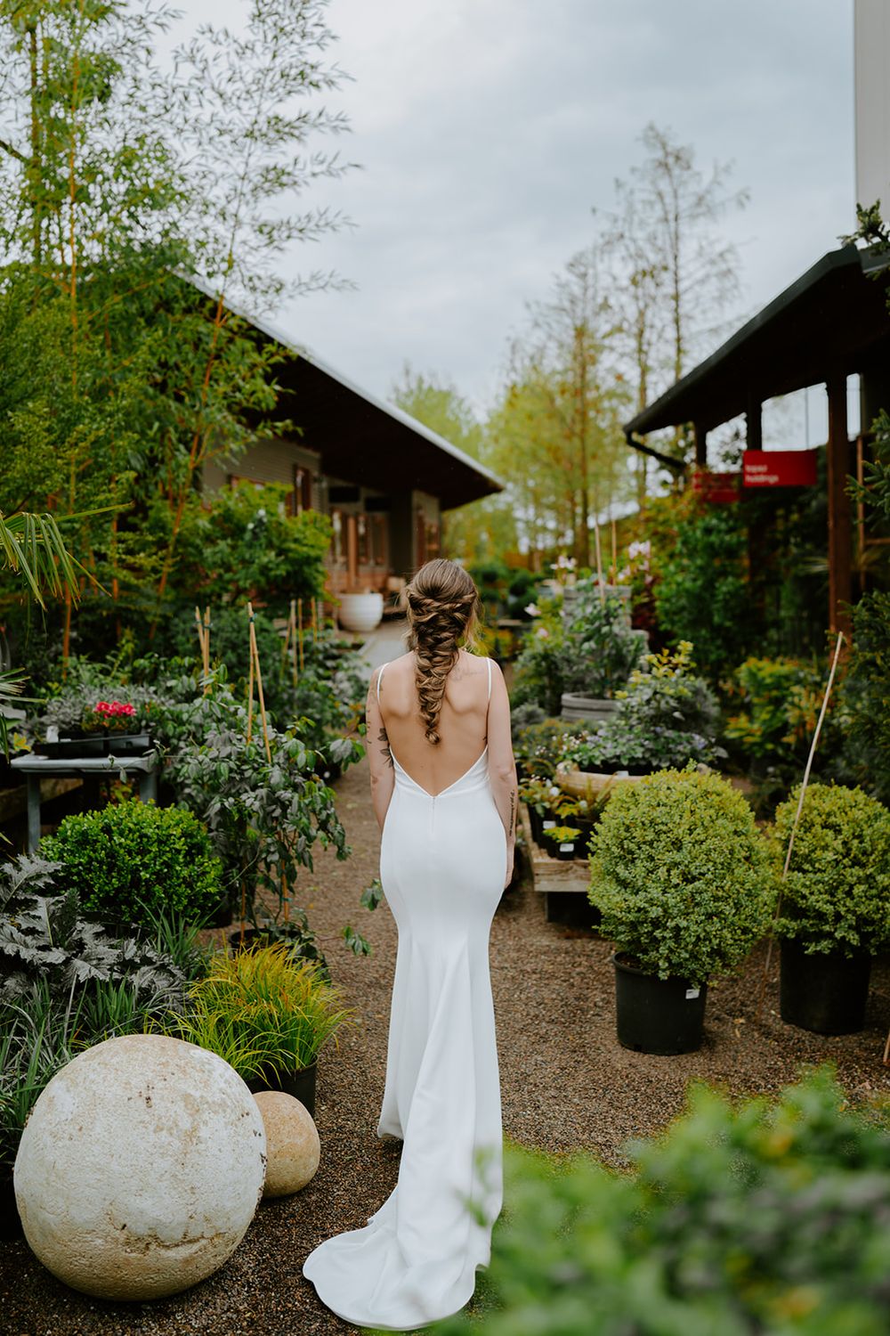 Fitted white wedding gown photographed in a lush garden nursery with decorative sphere ornaments.