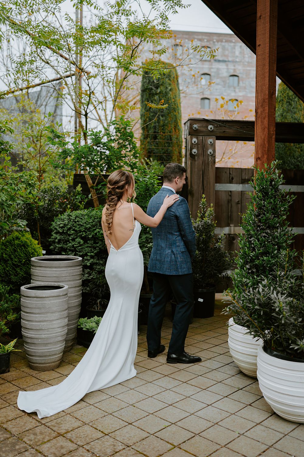 Couple sharing first look moment on stone patio surrounded by potted plants and greenery.