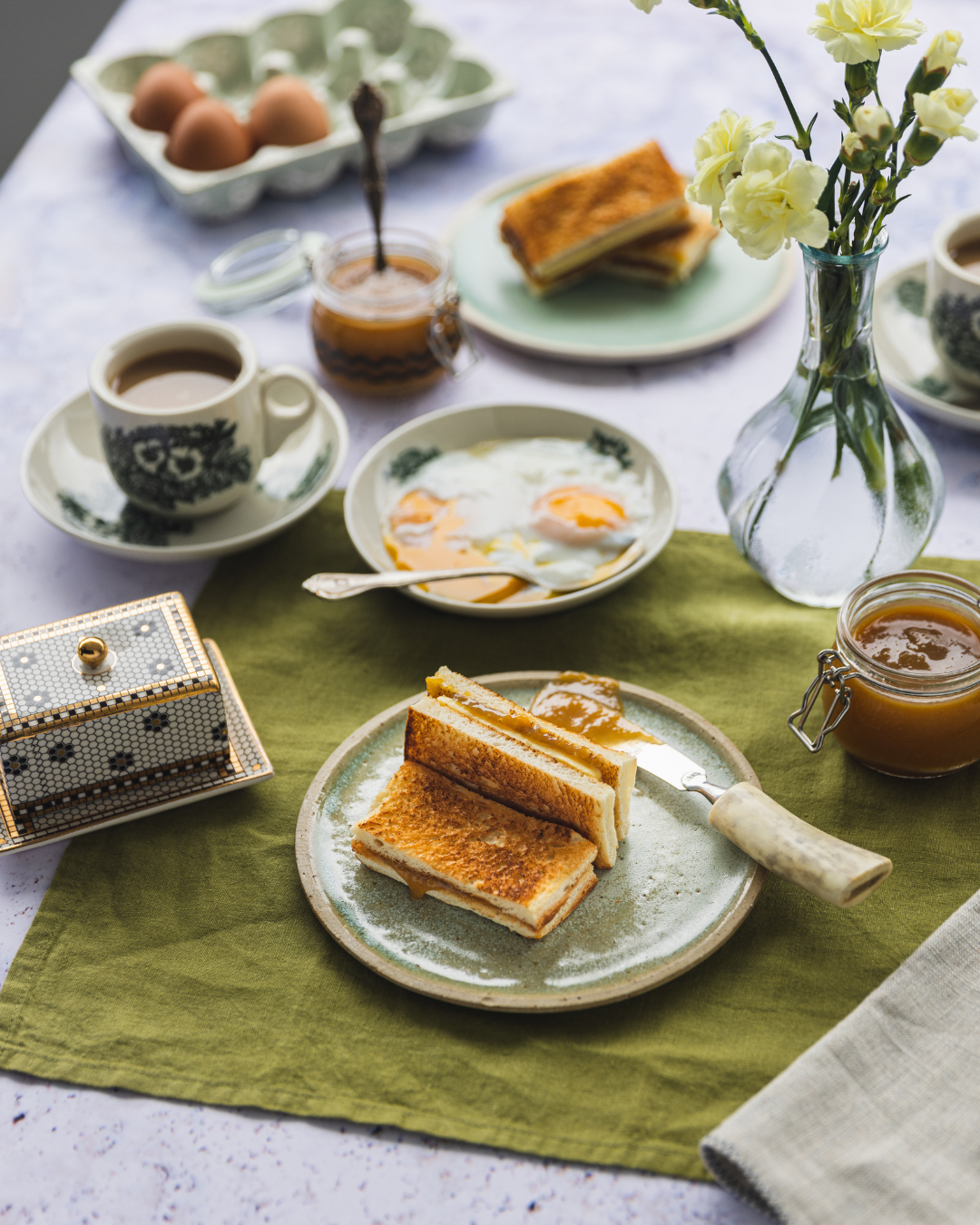 Breakfast table setting with toast, eggs, coffee, and fresh flowers in a vase on a green placemat.