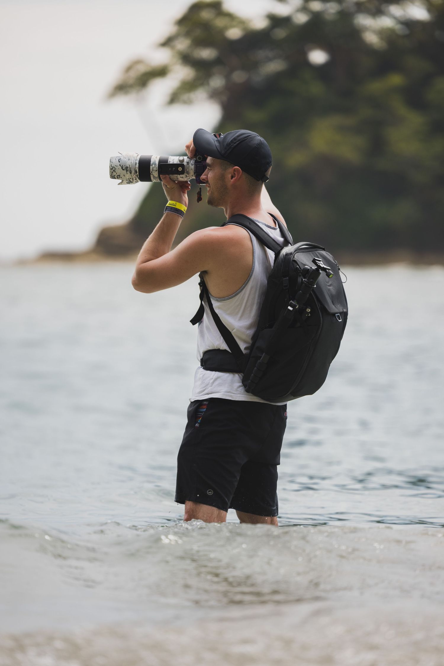 Photographer standing in ocean water taking pictures with professional camera and backpack.