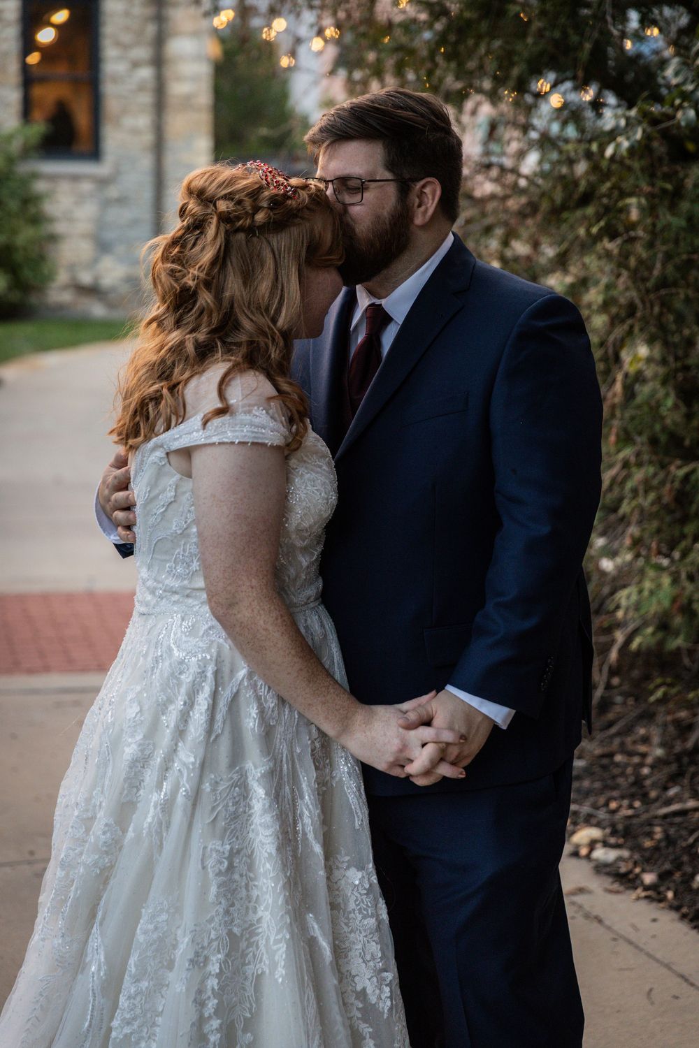 A couple shares an intimate moment in wedding attire, with the bride wearing a white lace dress and groom in navy suit.