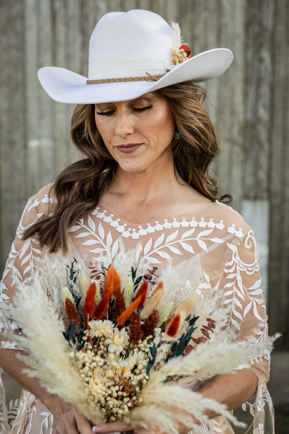 Bride in white cowboy hat holding dried flower bouquet with feathers and pampas grass.