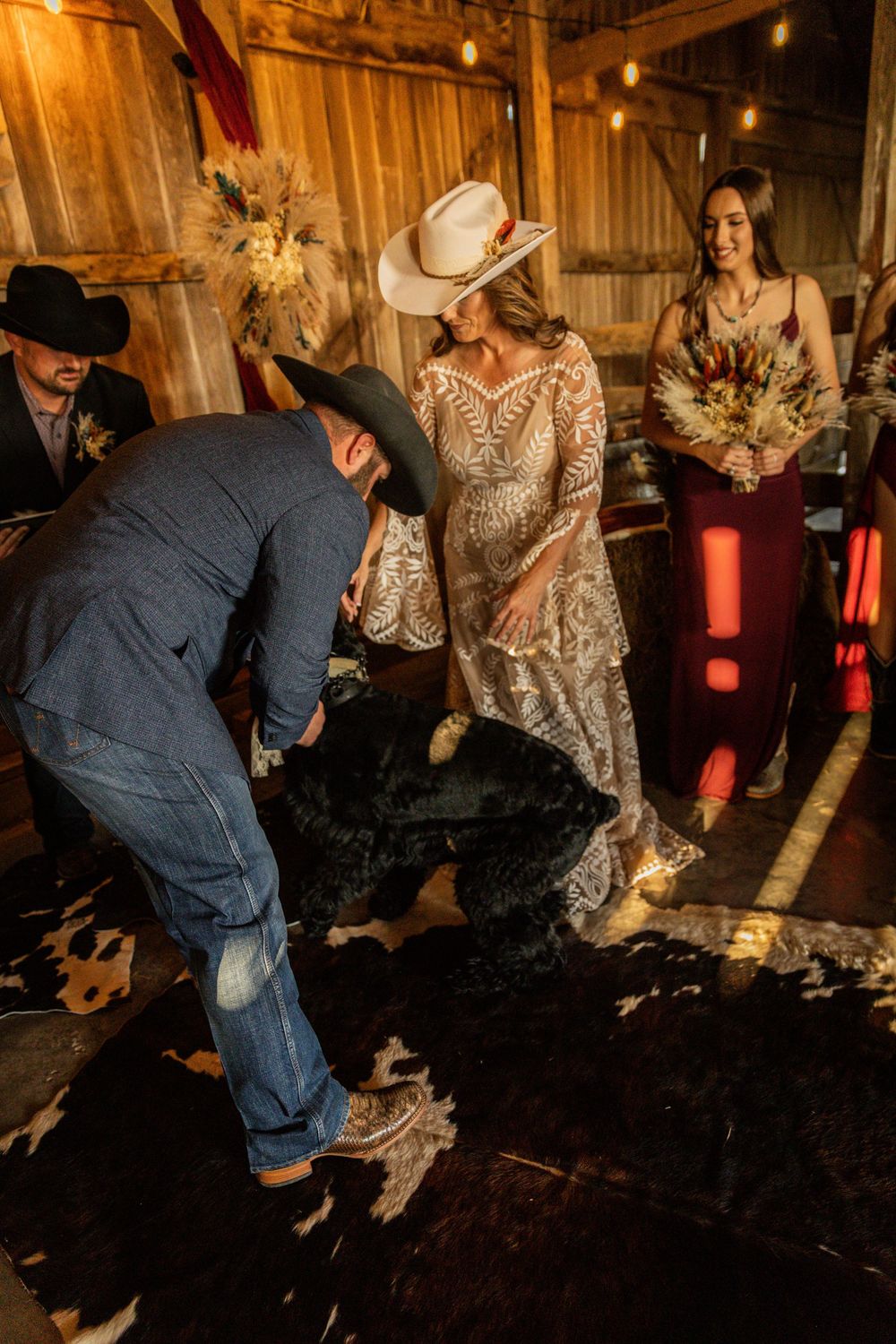 Wedding party dancing on rustic barn floor with string lights overhead.