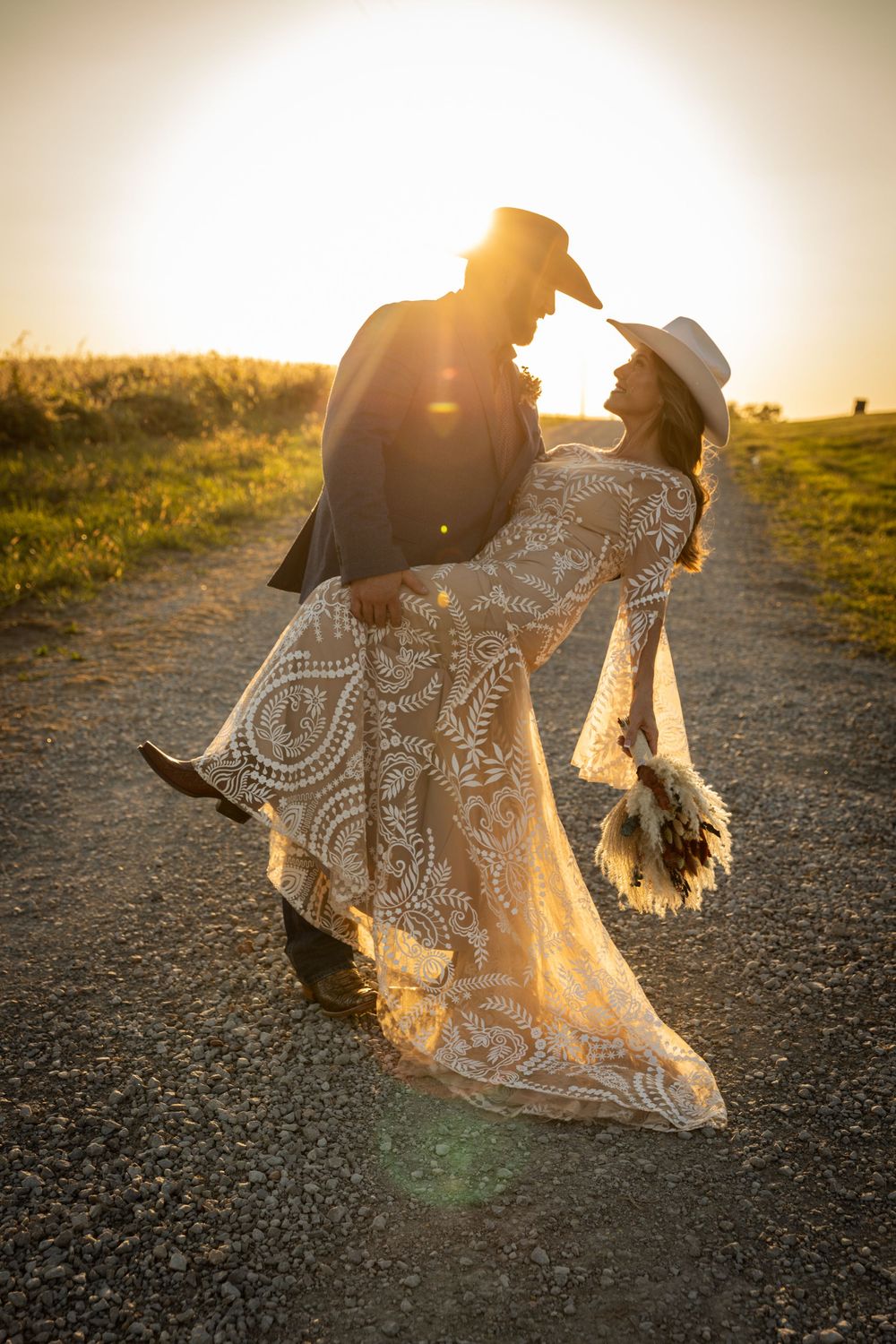 Golden sunset silhouettes couple on dirt path with lace dress flowing in breeze.