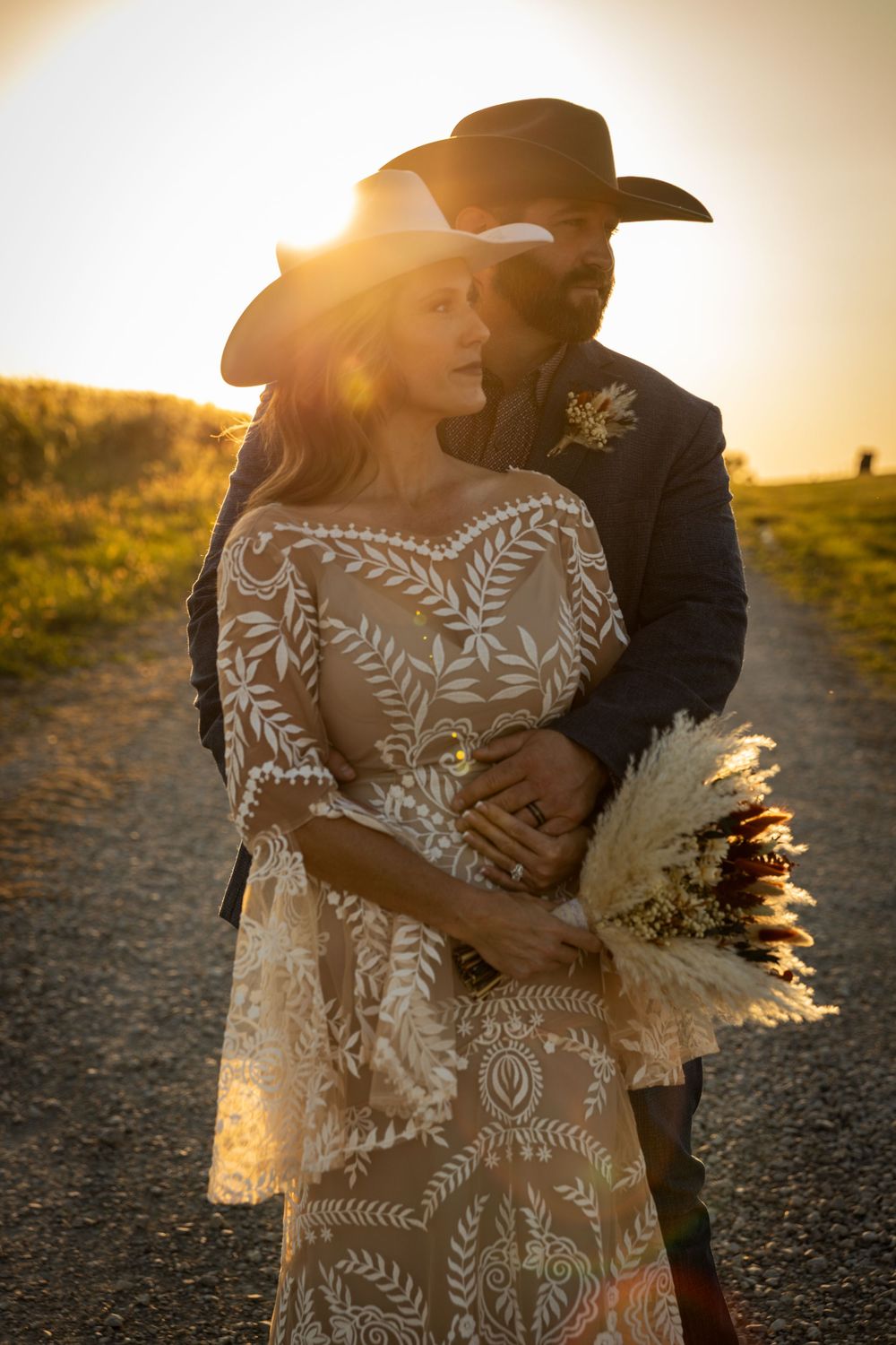 Romantic sunset portrait with cowboy hat and flowing lace dress on country path.