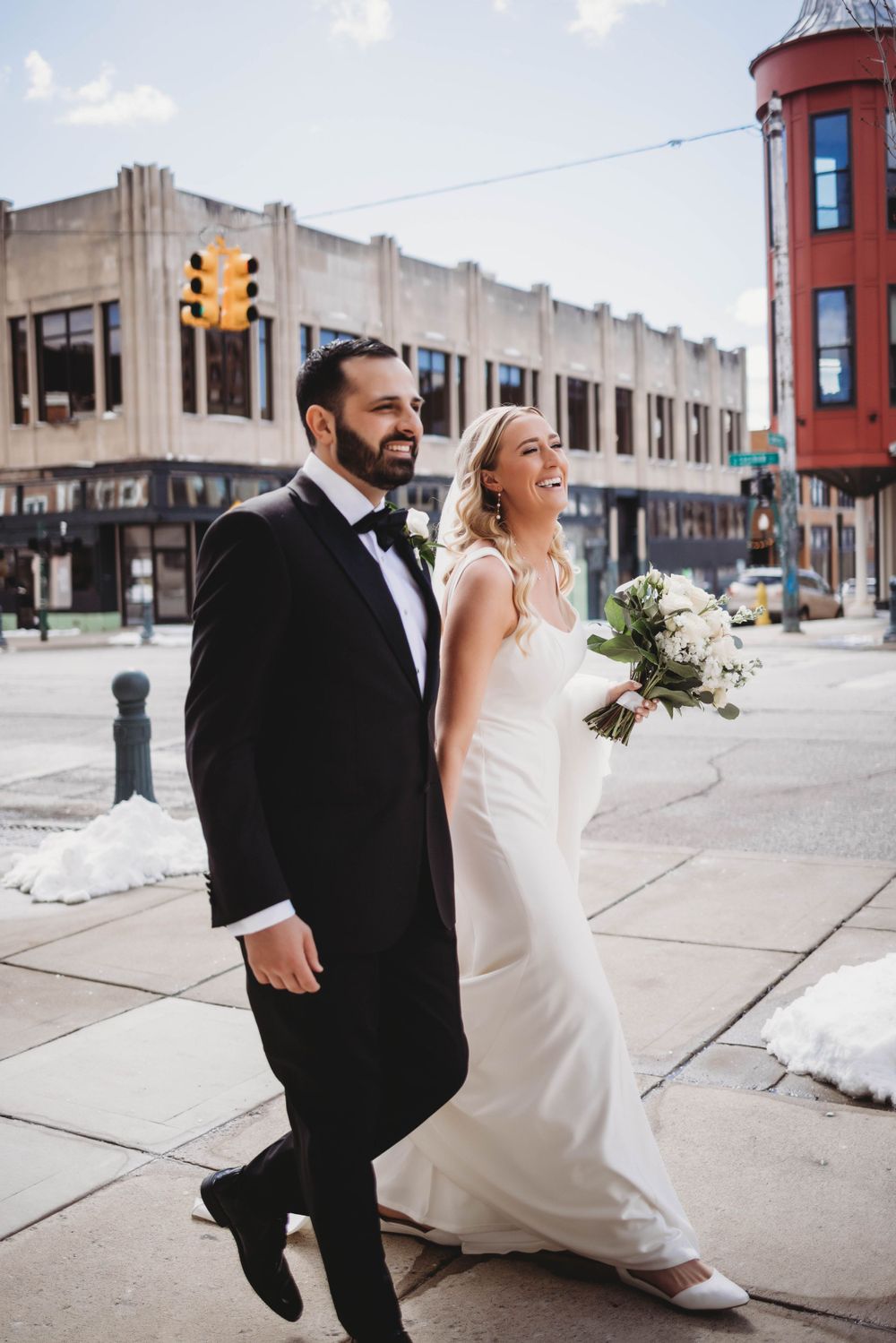 Bride and groom walking down urban street with classic architecture in background.