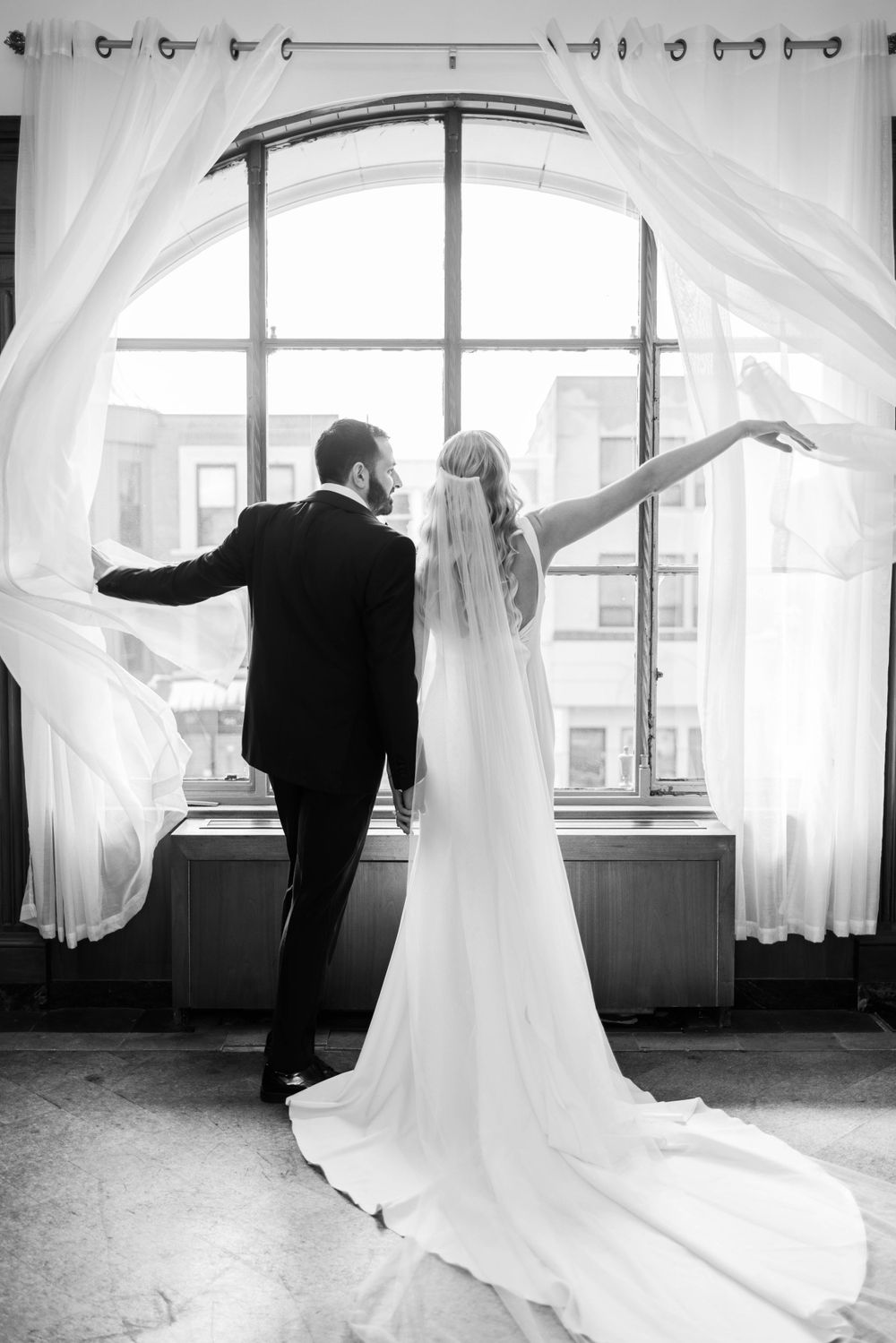 Silhouette of couple by window with flowing curtains and dramatic train of wedding gown.