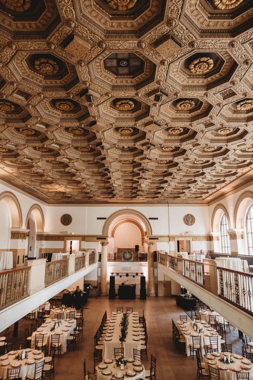 Ornate coffered ceiling over elegant wedding reception venue with round tables and classic decor.