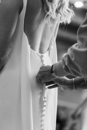 Black and white close-up of buttons being fastened on a wedding dress.