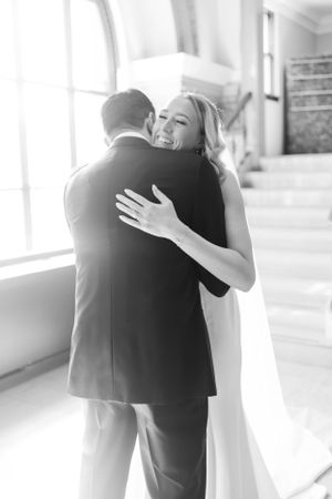 Black and white photo of tender embrace between newlyweds in sunlit venue.