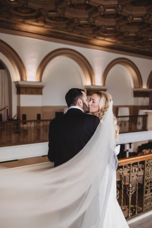 Romantic kiss between newlyweds under ornate arched ceiling.