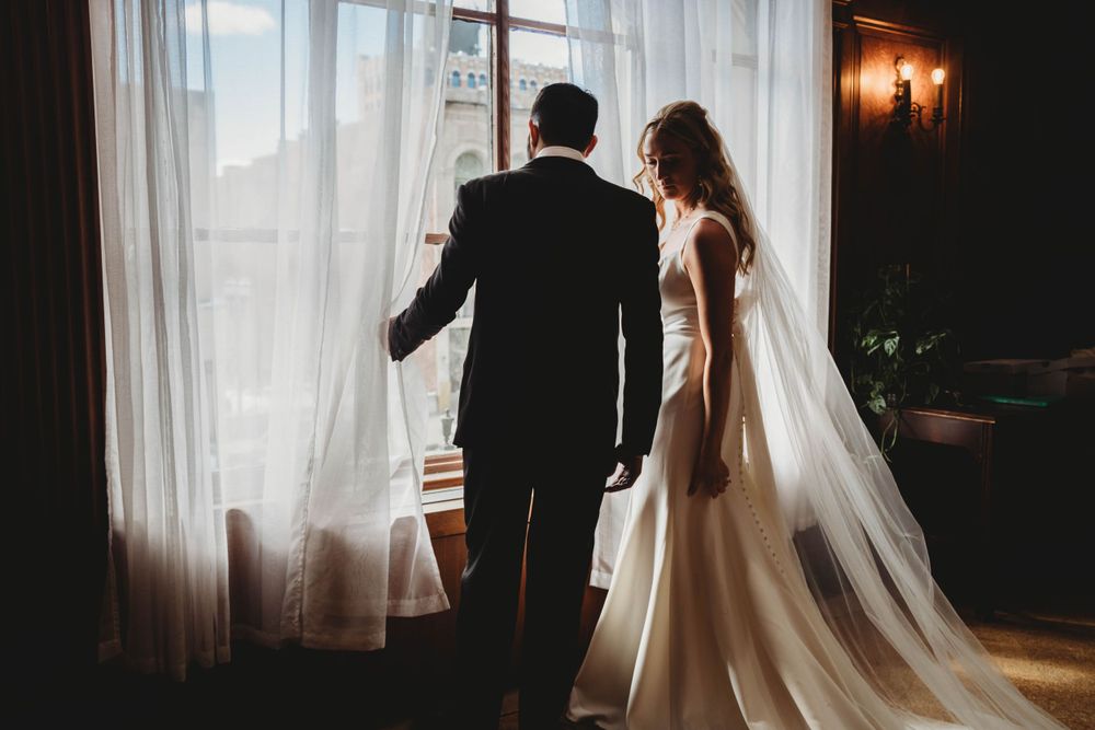 Silhouetted couple standing by window with flowing curtains and dramatic lighting.