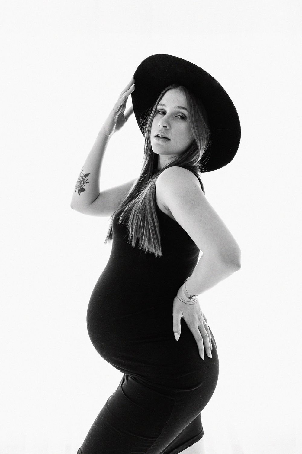 A silhouette of a pregnant woman in black poses dramatically wearing a wide-brimmed hat.