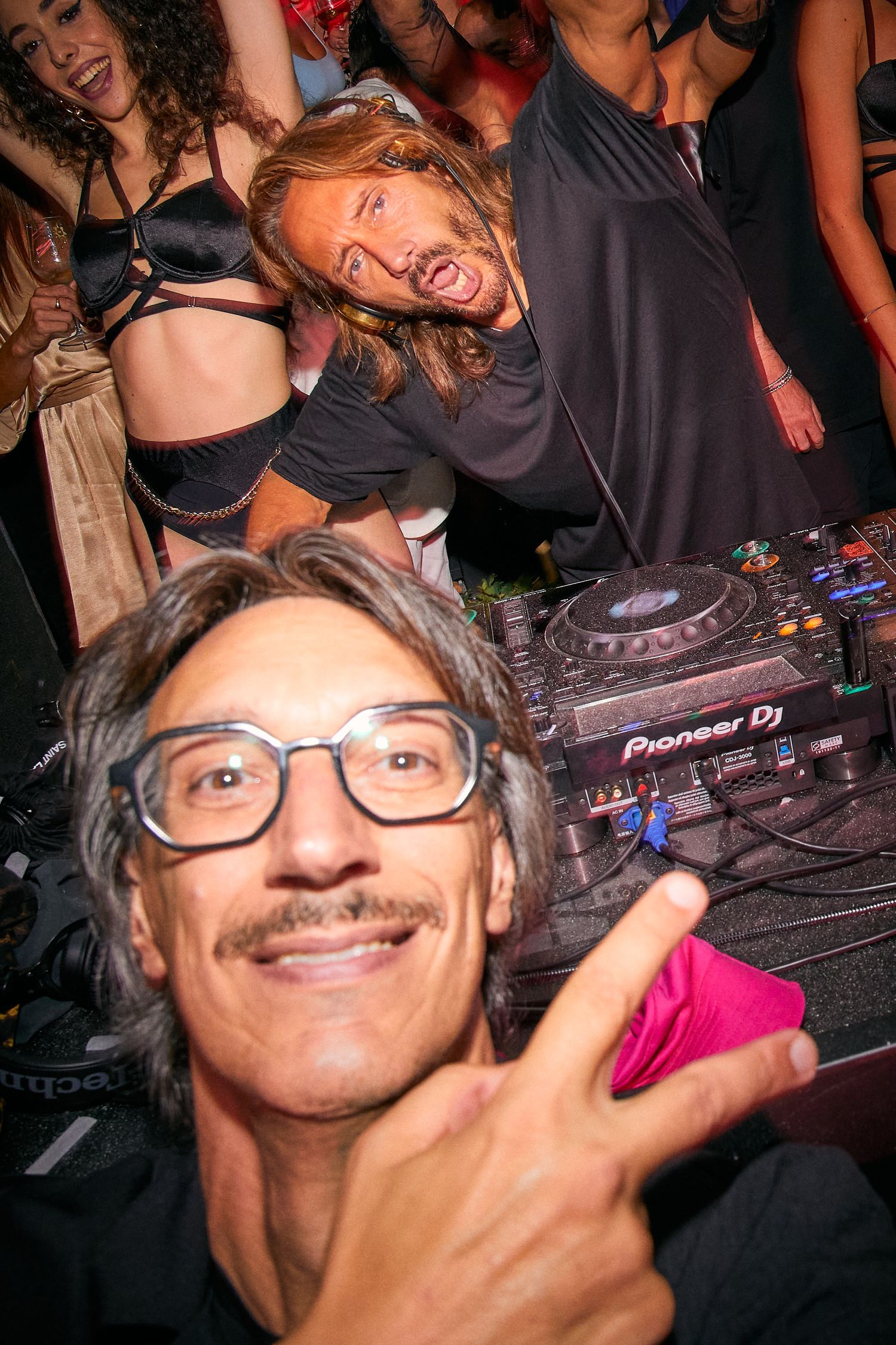 Energetic nightclub scene with DJ equipment and dancing crowd.