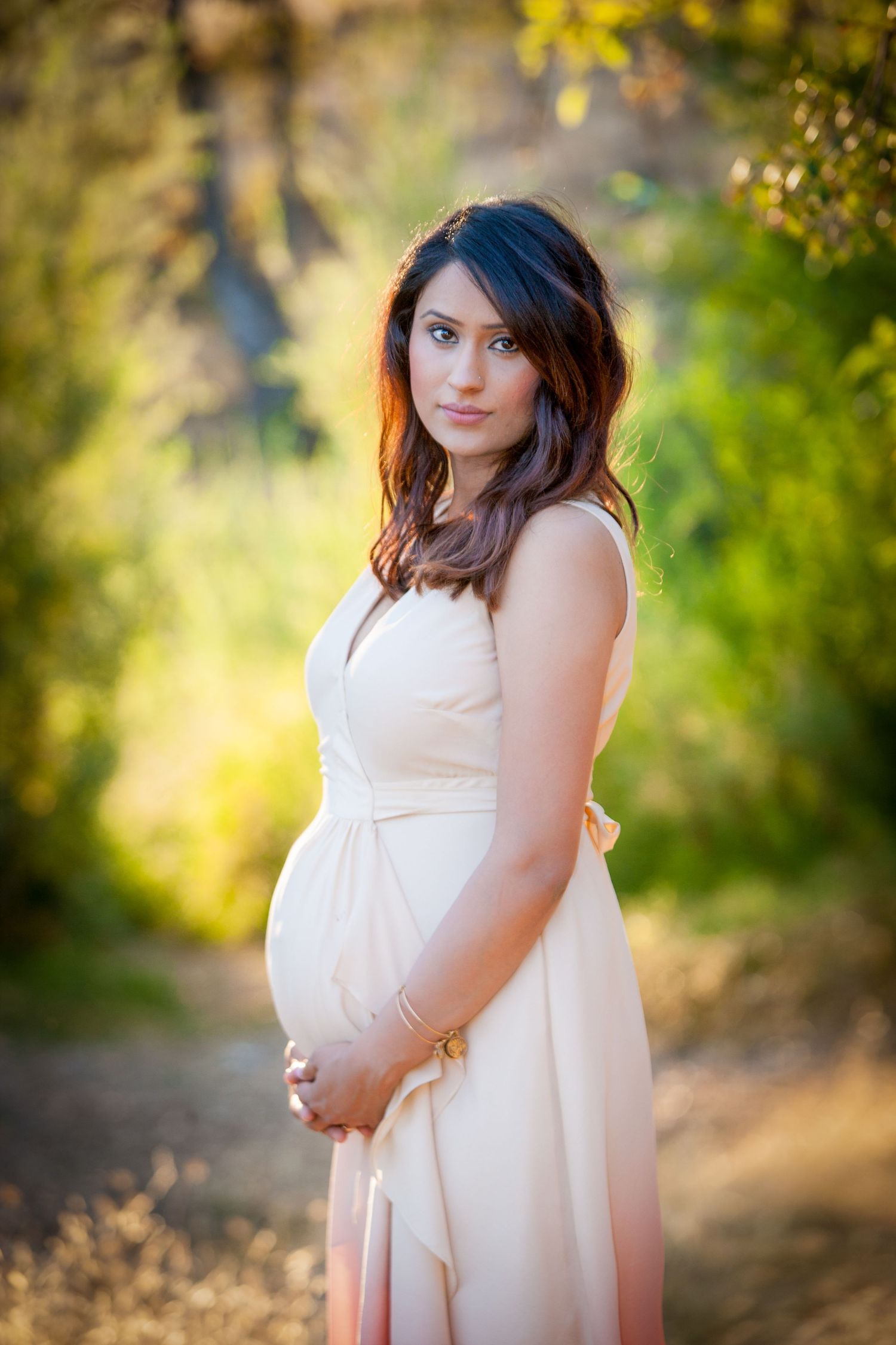 Maternity photoshoot in a natural outdoor setting with warm golden sunlight.