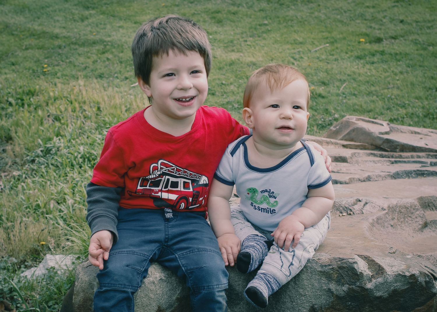 a young boy and a baby sitting on a rock