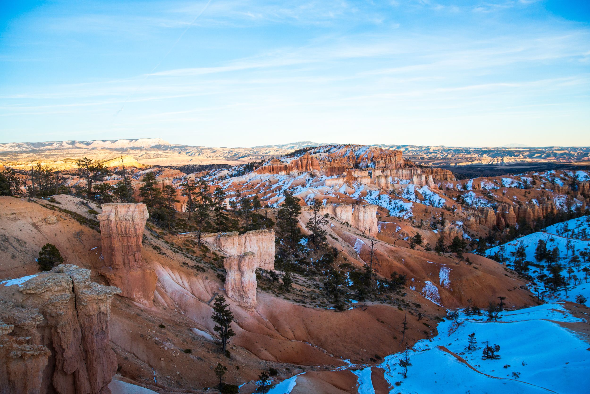 Snow-covered Bryce Canyon amphitheater with distinctive red rock hoodoos under bright blue skies.