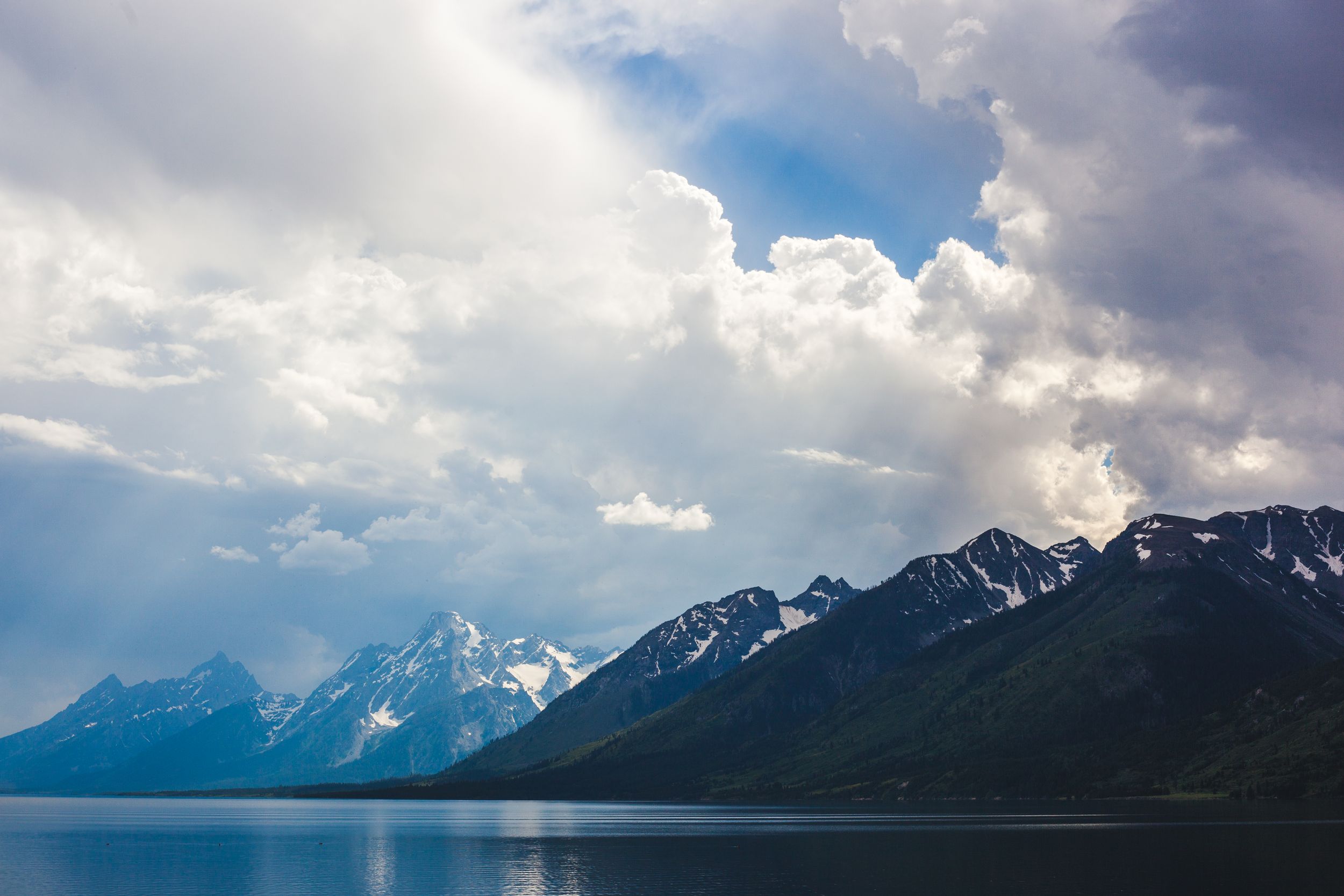 Panoramic mountain range landscape with dramatic cloudy sky and snow-capped peaks.