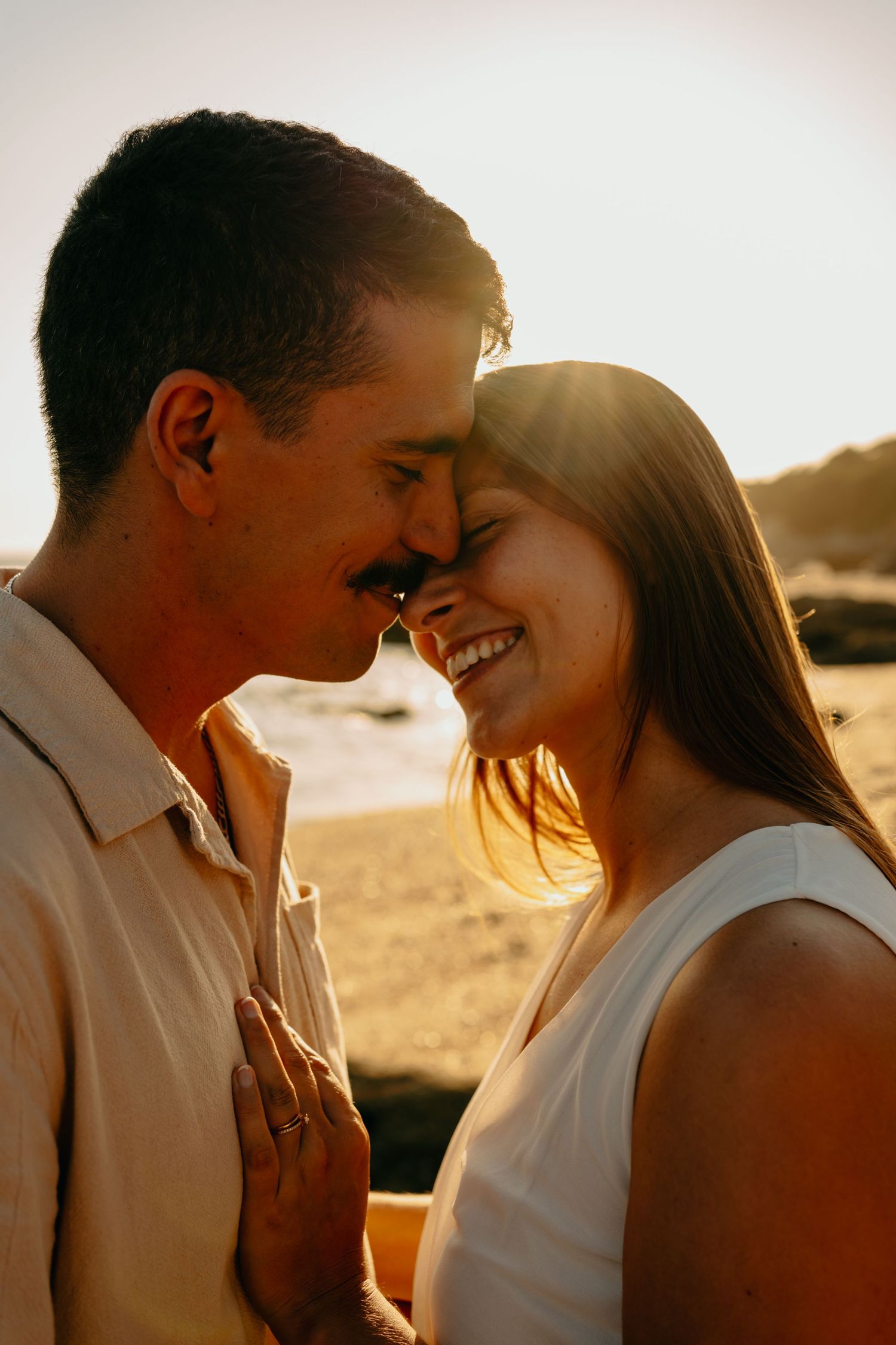 Romantic couple sharing intimate moments at sunset on the beach in warm golden light.