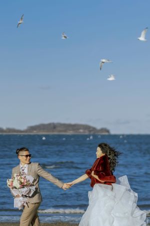 Romantic beach photoshoot with seagulls flying overhead and ocean waves in the background.