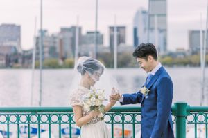 Couple standing on a waterfront promenade with city skyline in the background.